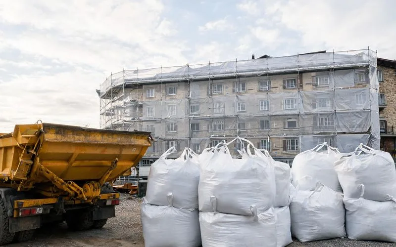 Big bags scellés de déchets amiantés et benne de chantier devant un immeuble en rénovation à Bienne