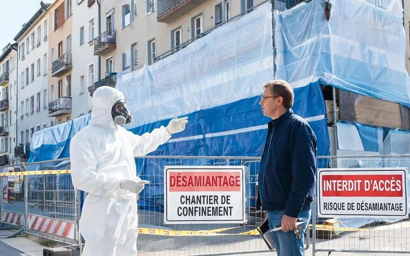 Chef de chantier d'une entreprise de désamiantage en combinaison blanche devant un immeuble à Bienne
